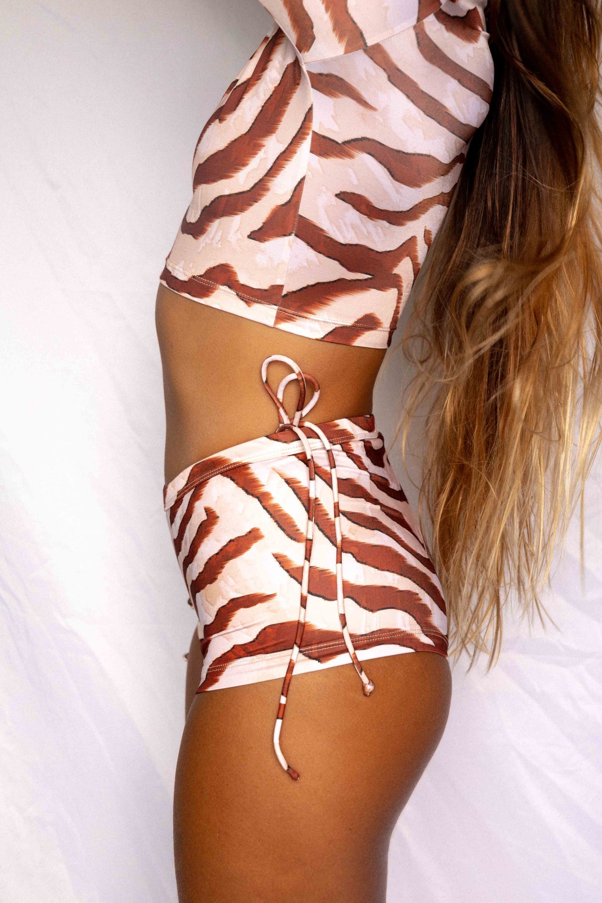 Lola Low-Rise Surf Shorts in Dune animal print, close-up side view showing side-tie detail and secure fit