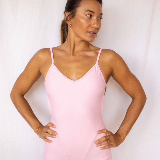 Elle Surf Suit in Blush — front view, model with hands on hips in soft pink one-piece with v-neckline and boyshort cut, Antidote The Label