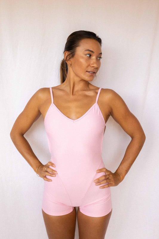 Elle Surf Suit in Blush — front view, model with hands on hips in soft pink one-piece with v-neckline and boyshort cut, Antidote The Label