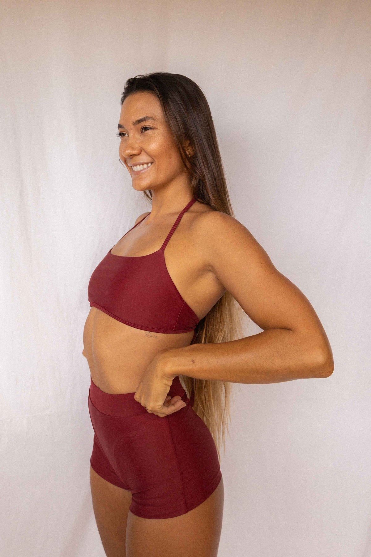 Niki Surf Top and Shorts set in Deep Merlot, smiling side profile view showing thin strap top and high-waist shorts by Antidote The Label
