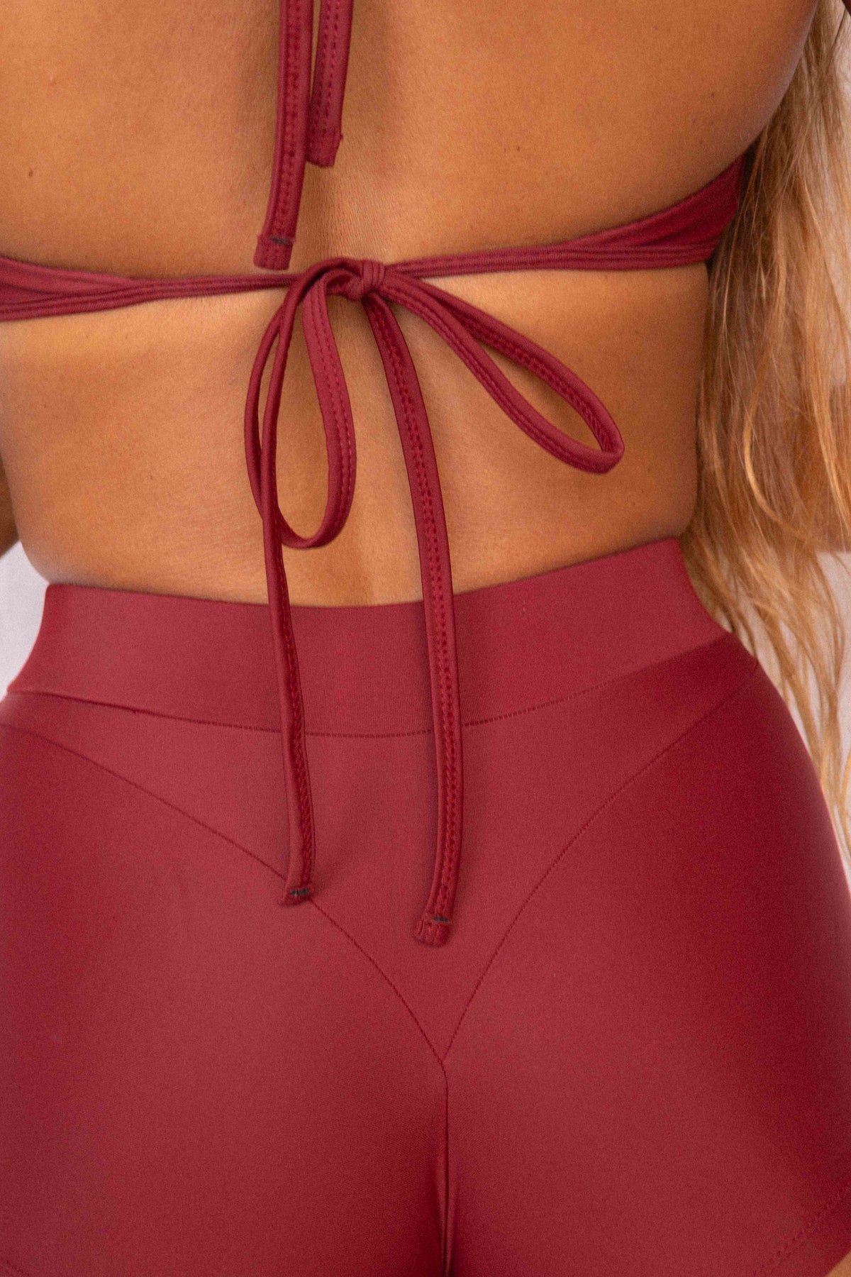 Niki Surf Shorts in Deep Merlot, close-up back detail showing V-seam waistband construction and lower back tie of matching surf top