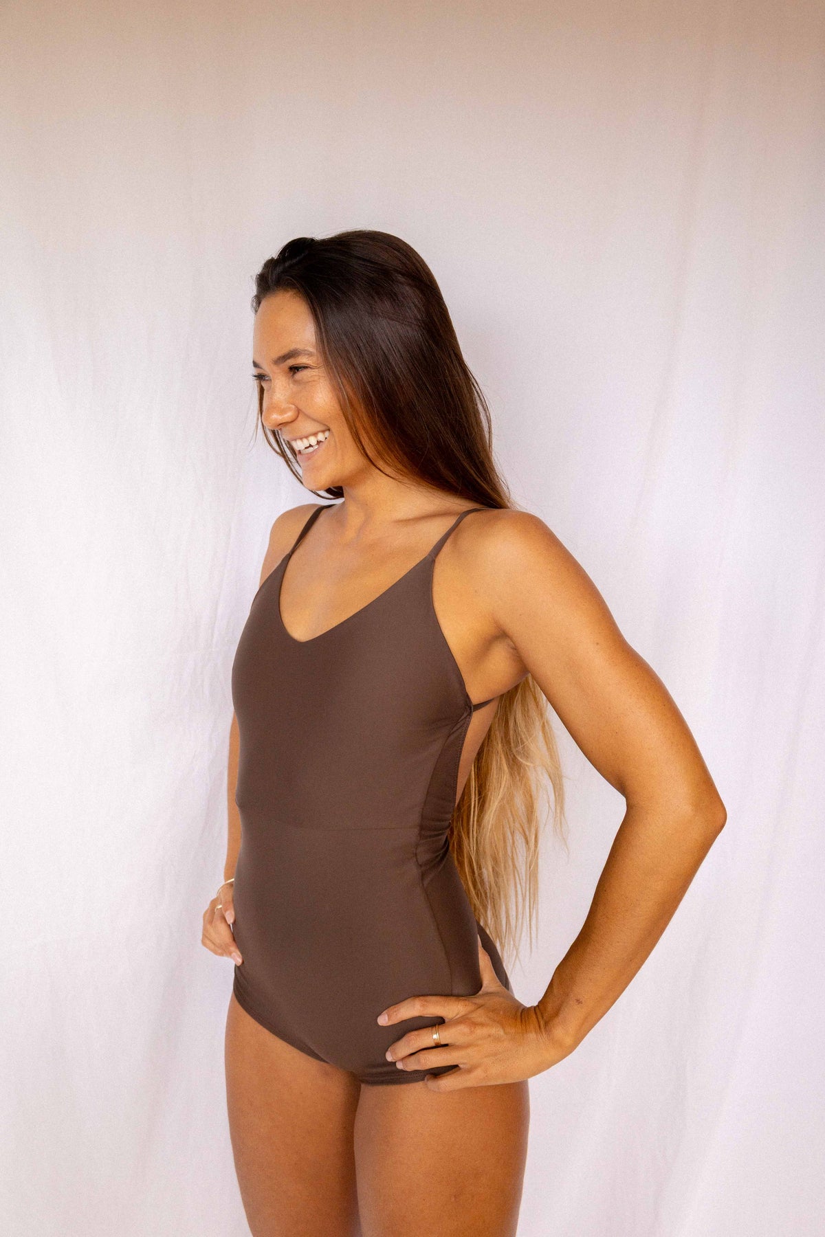 Emi Surf Suit in Coffee — front view, model smiling in earth-tone one-piece swimsuit with thin straps, Antidote The Label