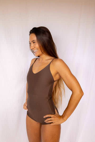 Emi Surf Suit in Coffee — front view, model smiling in earth-tone one-piece swimsuit with thin straps, Antidote The Label