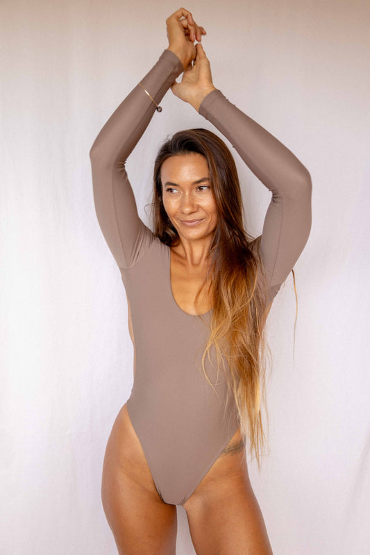 Nia Long-Sleeve Surf Suit in Taupe, front view with arms raised showing scoop neckline, long-sleeve construction and high-cut one-piece silhouette by Antidote The Label