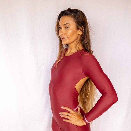 Anou Long-Sleeve Surf Suit in Deep Merlot, side profile showing open back cutout and streamlined long-sleeve one-piece silhouette