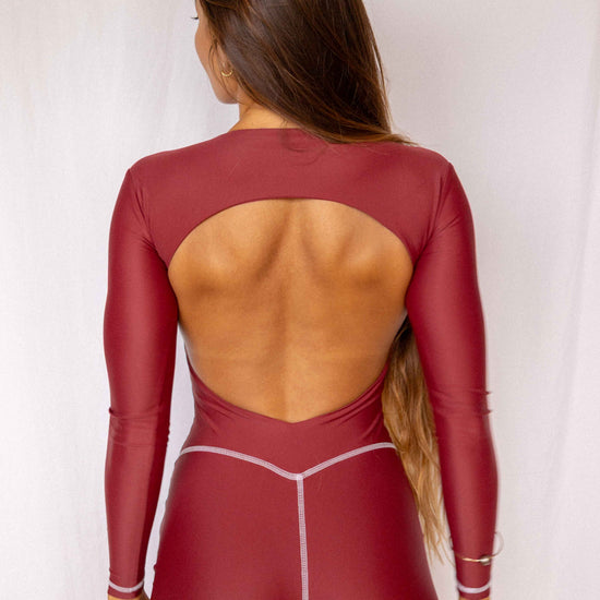 Anou Long-Sleeve Surf Suit in Deep Merlot, full back view showing open back cutout, long sleeves, and contrast stitch short construction