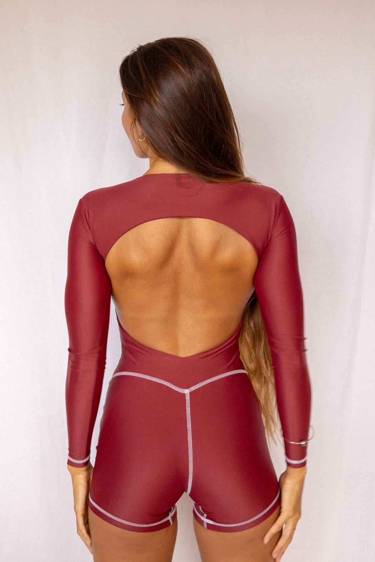 Anou Long-Sleeve Surf Suit in Deep Merlot, full back view showing open back cutout, long sleeves, and contrast stitch short construction